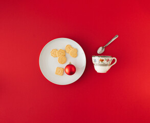 Minimal composition with Christmas cookies and red bauble on white plate and tea cup with spoon. New year concept.