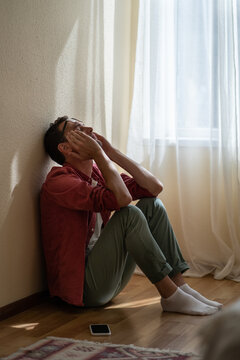 Upset Depressed Young Man Sitting With Closed Eyes On Floor At Home, Getting Unexpected Bad News Over Phone. Frustrated Guy Suffering From Relationship Break Up, Cannot Forget About Ex-girlfriend