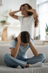 Depressed teenage girl covering ears with hands while her frustrated angry mother yelling on...