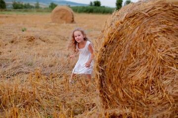 Naklejka na ściany i meble a red-haired girl in a white dress with curls contorts her face at a haystack