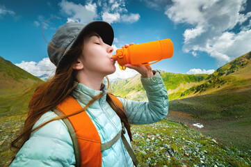 Young sports girl stands against the backdrop of a stunning mountain view and drinks clean water...