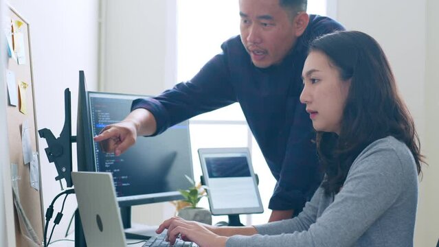 Young Asian man, developer programmer, software engineer, IT support, with colleague discuss and working on computer to check coding in bugging system