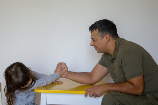 Image of a young dad playing arm wrestling with his daughter. Struggle between parents and children
