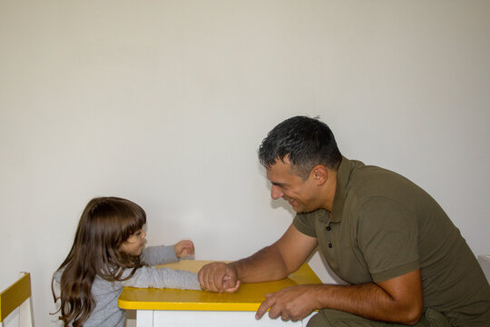 Image of a young dad playing arm wrestling with his daughter. You play at home and the dad wins a showdown
