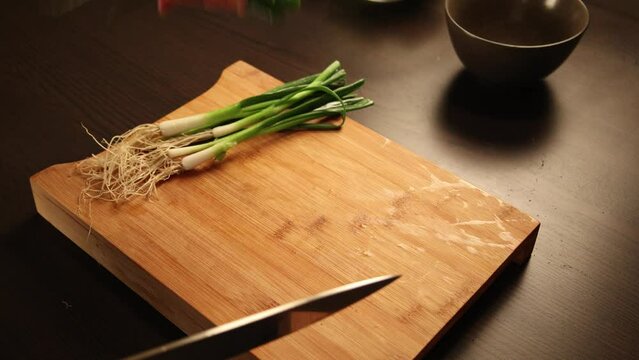 woman hands cutting green onion close up on wooden board at home