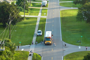 Aerial view of american yellow school bus picking up children at sidewalk bus stop for their...