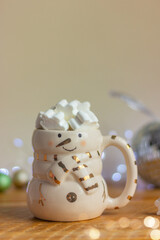 close up of a snowman cup with white marshmallow snowflakes on a table against a background of holiday lights