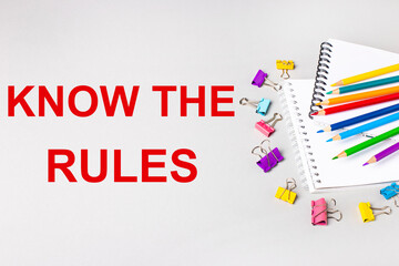Notebooks, colored pencils and paper clips on a light gray table. The inscription KNOW THE RULES. Banner
