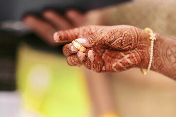 Close-up hand of Indian woman bride with a gold bracelet and henna drawings, holding wedding ring...