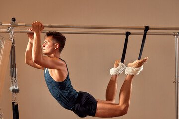 Fototapeta premium Fit man doing a lunge stretch yoga pilates exercise to strengthen and tone his muscles using a reformer in a gym