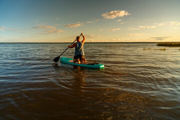 Fototapeta premium a man in shorts with a paddle on a sup board at sunset in the lake.
