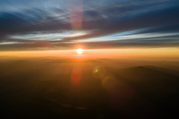 Aerial view of dark mountain hills with bright sunrays of setting sun at sunset. Hazy peaks and misty valleys in evening