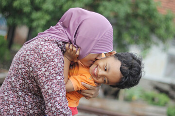 A mother kisses her adorable smiley son on a deliberately blurred background . Selective focus