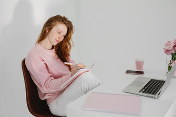 Relaxed pensive young woman sitting at workplace in office and making notes.