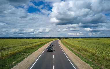 Aerial view of intercity road between green agricultural fields with fast driving cars. Top view from drone of highway traffic