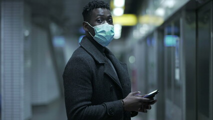 Black man standing at subway platform wearing coronavirus face mask prevention