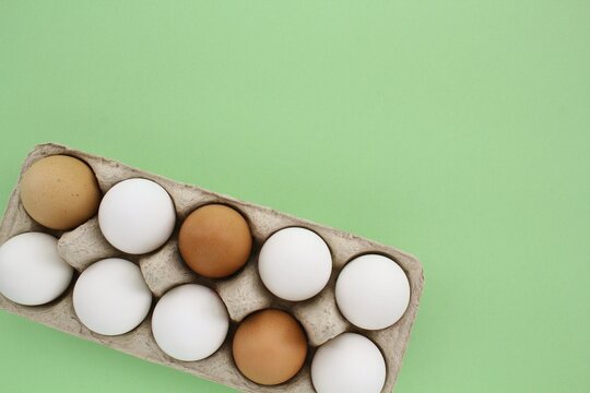 Fresh white and brown chicken eggs in carton paper box on green background. Natural healthy nutrition organic farm food product concept. World egg day, easter holiday composition. Copy space, flatlay