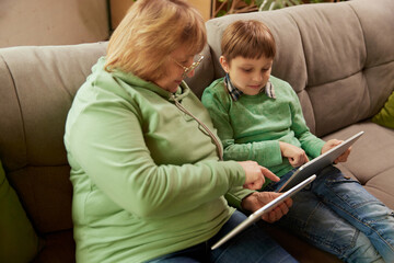 Middle age woman and school age boy, granny and grandson sitting at home and talking, having fun. Concept of emotions, family, happiness, care, support and leisure activities
