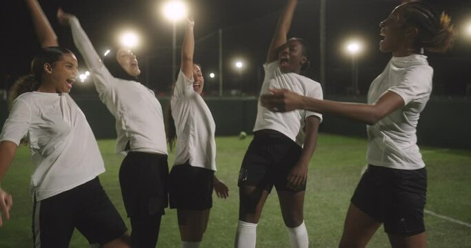 Female soccer team in stacking hands in soccer field at night