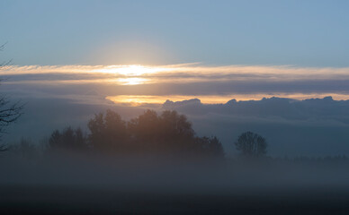 Over a foggy meadow in the south of Augsburg clouds rise in the shape of a mountain range
