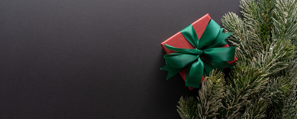 close up on red gift box with rolling ribbon on black background with pine leaves and copy space...