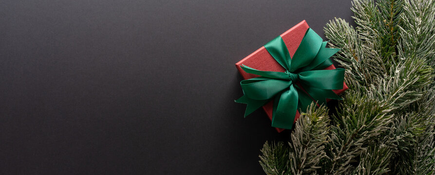 close up on red gift box with rolling ribbon on black background with pine leaves and copy space for merry christmas, happy new year ,festival ,birthday and anniversary, concept design