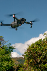 Small drone flying over trees with blue sky as background