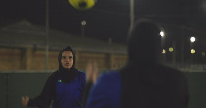 Female soccer players in hijabs throwing ball in soccer field at night