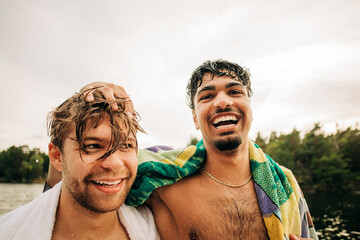 Portrait of happy man with towel by male friend during vacation