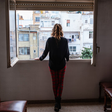 Rear View Of Woman Standing By Window At Home