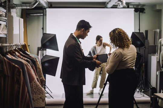Side view of male designer discussing with female photographer in studio - Powered by Adobe