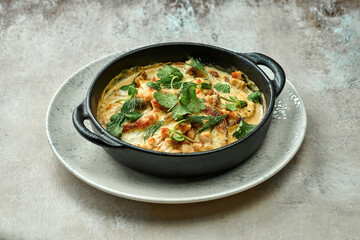 Baked draniki in cream sauce with bacon on a plate on a textured background. Close-up, selective focus