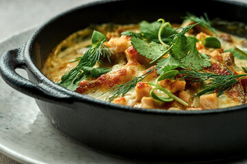Baked draniki in cream sauce with bacon on a plate on a textured background. Close-up, selective focus