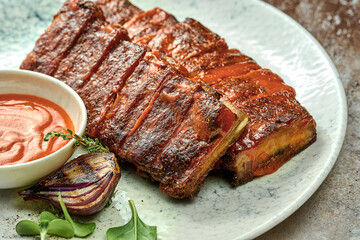 Baked barbecue ribs with mango sauce in a white plate on a textured background. Close-up, selective focus
