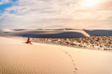 Young woman person sitting on famous white sands dunes national monument in New Mexico on disk sled for sliding down hill during sunset with vintage brown yellow tone