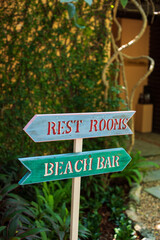 Close up of painted wooden signs in a resort hotel. Showing rest rooms to the left and beach bar to the right. 