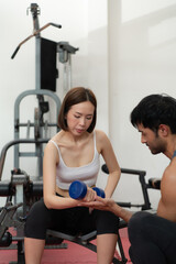 Fototapeta premium Young couple exercising in a gym When lifting weights, they assist one another. Concept of bodybuilding and healthy living
