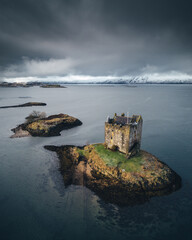 Dramatic weather at Castle Stalker, snowcapped mountains in the distance, Scottish Highlands. North Coast 500, NC500.  