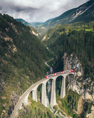 Red Train going over Landwasser Viaduct, Switzerland. Tall mountains with Train on bridge beneath
