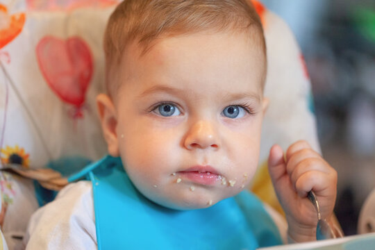 Closeup portrait of happy smiling baby eating in highchair at kitchen. Infant kid eating healthy nutrition on high chair.