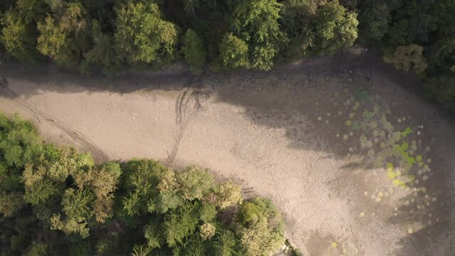 Dried up river bed with remains of dirty water in puddles, located in the forest area, aerial above view.