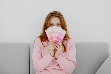 Woman sitting on sofa and hiding behind pink paint swatches.