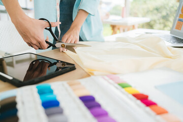 Close up hand of tailor or fashion designer cutting fabric with scissors for making a pattern of clothes. Fashion designer tailor or sewer in the workshop working for new collection clothes.