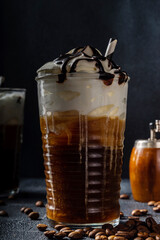 Cold coffee drink frappe (frappuccino), with whipped cream and chocolate syrup, with straws, coffee beans on a dark gray stone table, copy space 