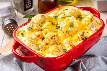 Loaded cheesy vegetable cauliflower casserole, with creamy sauce, baked autumn vegan dish, on light tiled background copy space - obrazy, fototapety, plakaty