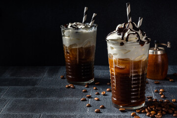 Cold coffee drink frappe (frappuccino), with whipped cream and chocolate syrup, with straws, coffee beans on a dark gray stone table, copy space 