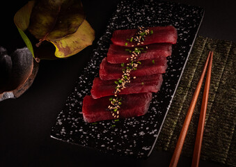 Sashimi tuna, delicious Japanese food with black background and decorated with leaves and soy sauce, for oriental and Asian food restaurant.