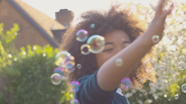 Smiling boy outdoors having fun playing with bubbles in garden -shot in slow motion