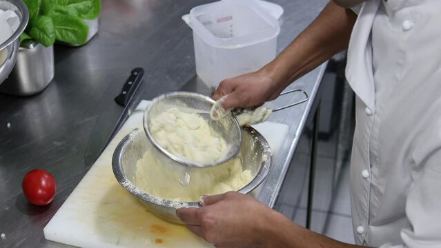 Chef's hands sifting some baby squids in flour with a colander to later fry them