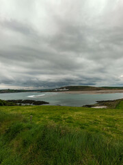 Thick green grass on a hill near the sea bay. Cloudy sky over Clonakilty Bay, seascape. View from above.